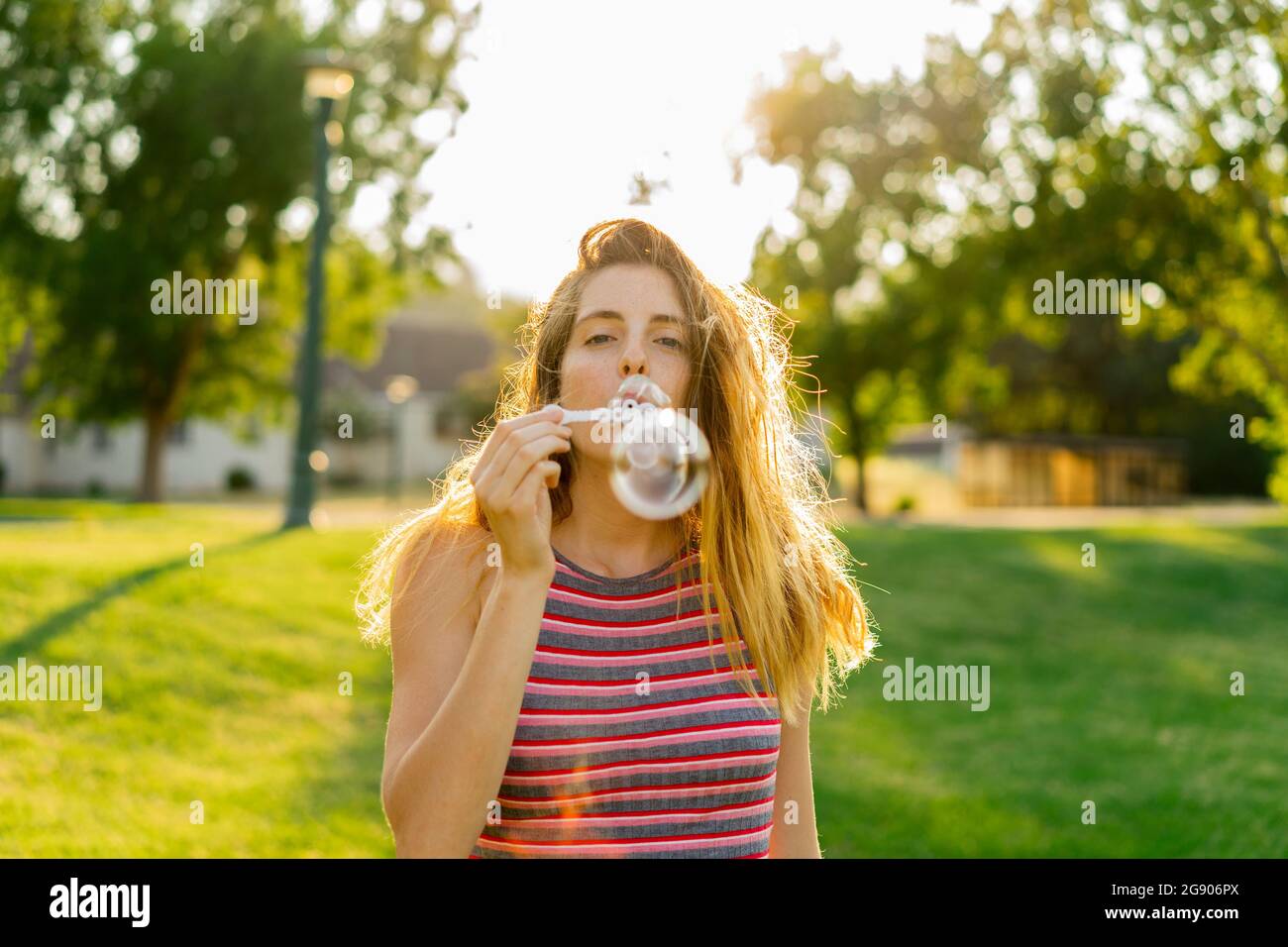 Junge Frau, die Blasen bläst und im Park steht Stockfoto