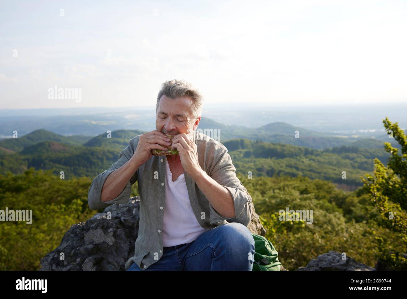 Männlicher Wanderer, der Essen isst, während er auf dem Berg sitzt Stockfoto