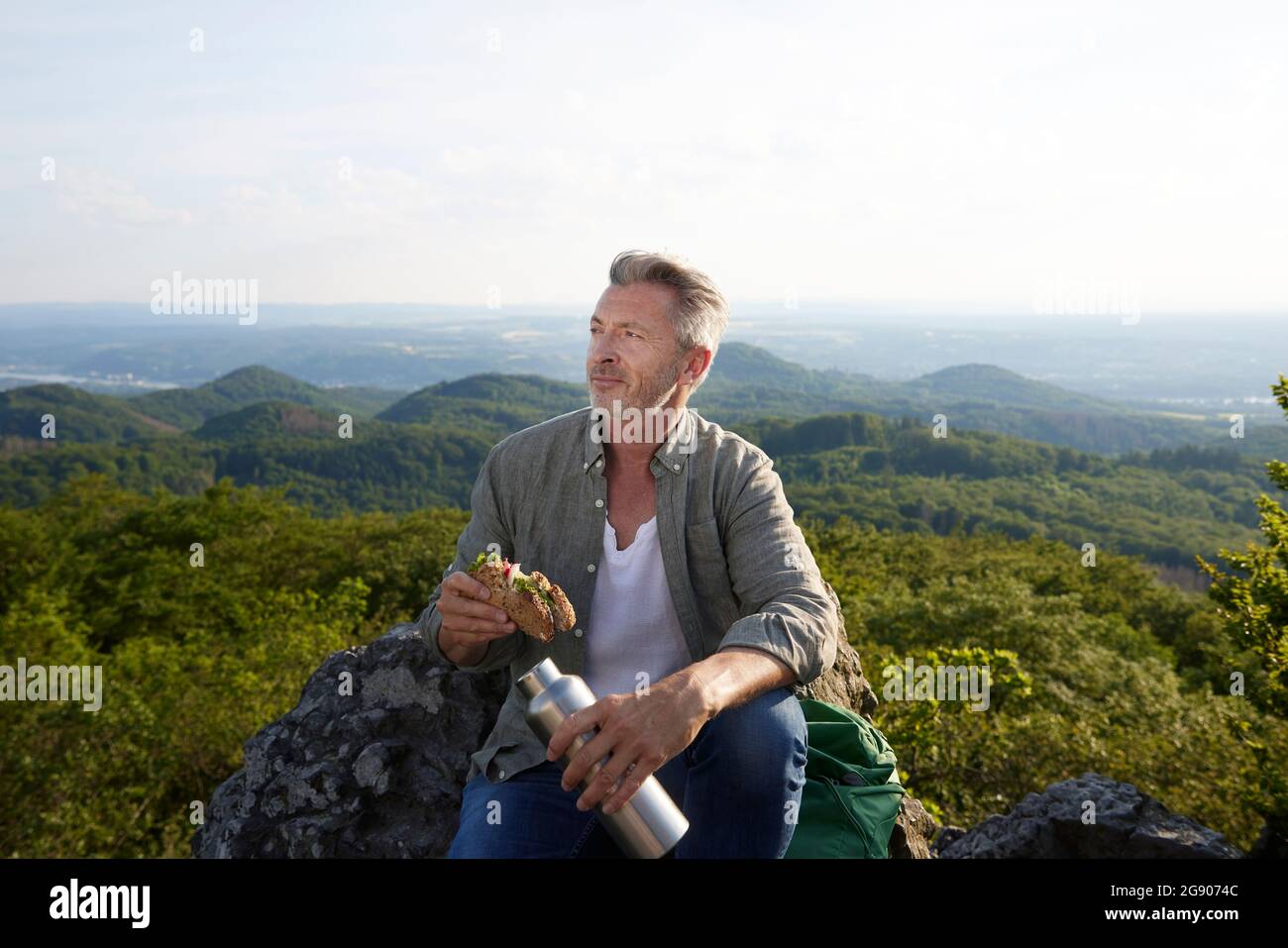 Männlicher Wanderer mit Essen und Flasche sitzt auf dem Berg Stockfoto