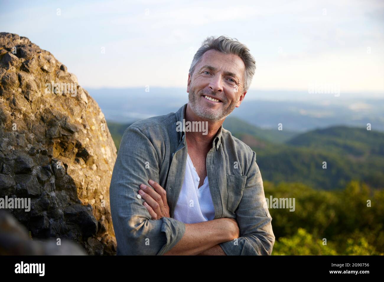 Männlicher Wanderer, der bei Sonnenuntergang lächelt und die Arme kreuzt Stockfoto