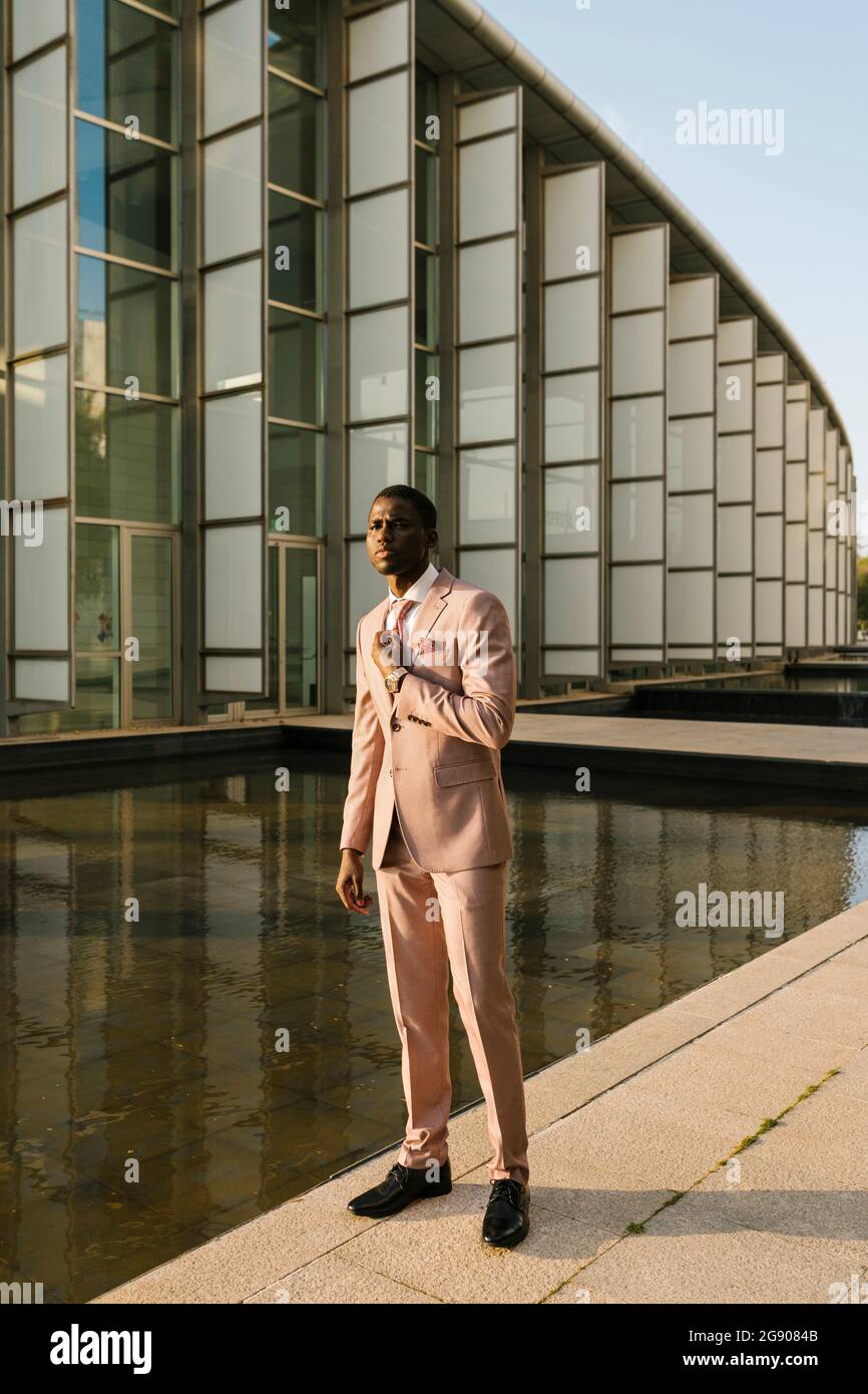 Eleganter Mann mit Anzug, der auf dem Fußweg am Teich steht Stockfoto