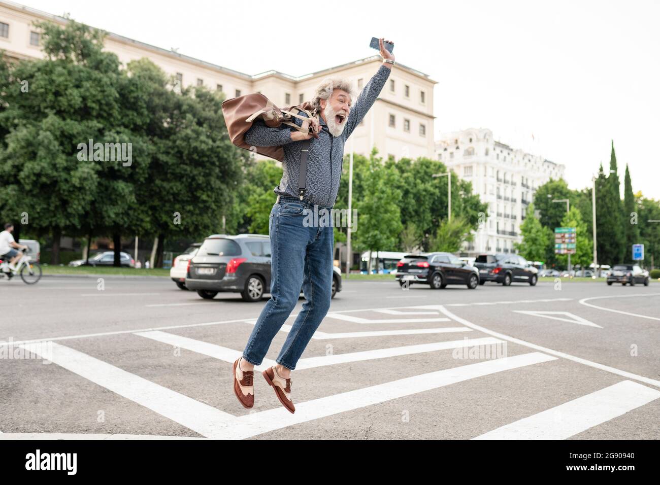 Aufgeregt reifer Mann, der Gepäck trägt, während er vor Freude auf der Straße hüpft Stockfoto