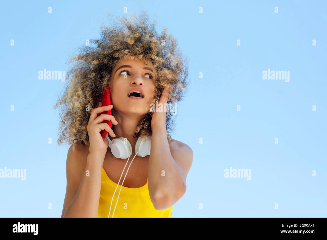 Junge Frau mit offenem Mund hört Handy Stockfoto