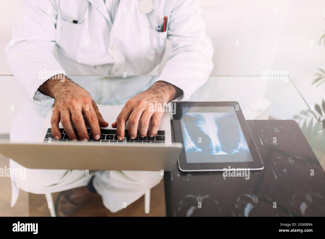Leitender männlicher Arzt, der am Schreibtisch in der Klinik am Laptop arbeitet Stockfoto