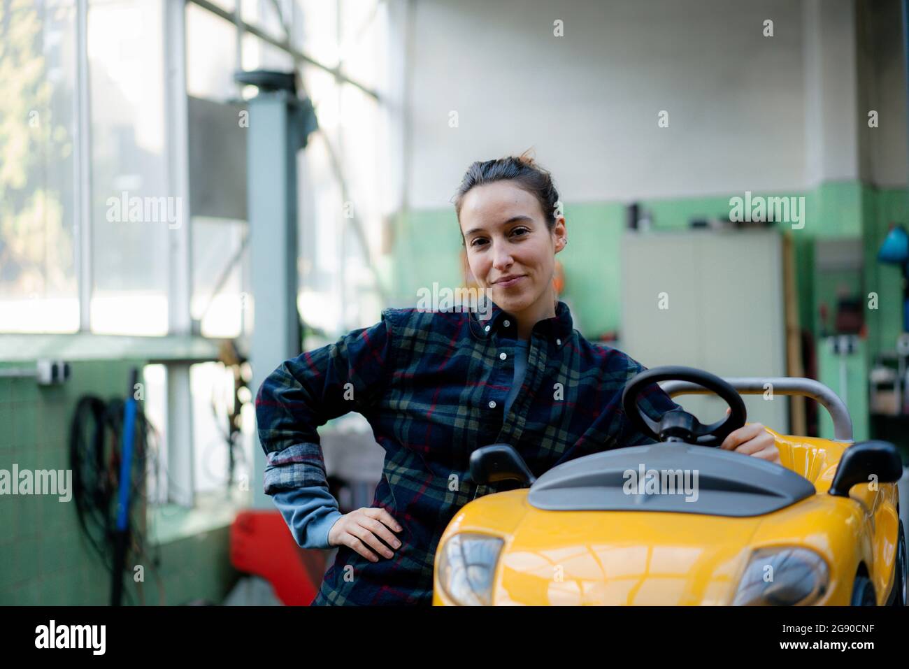 Mechanikerin mit der Hand auf der Hüfte, die sich in der Werkstatt auf ein Spielzeugauto stützt Stockfoto