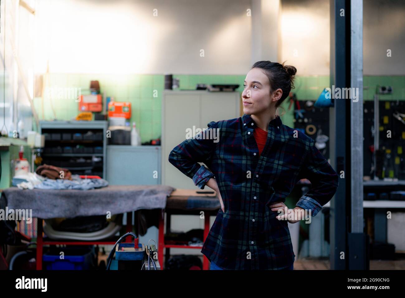 Mechanikerin mit der Hand auf der Hüfte, die in der Werkstatt wegschaut Stockfoto
