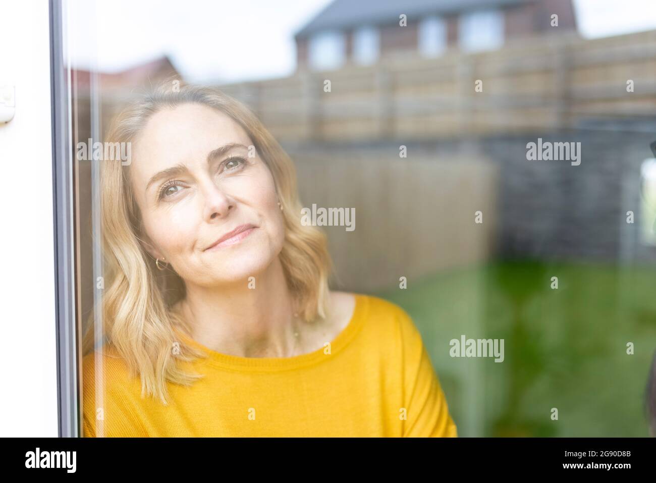 Frau, die zu Hause durch das Glasfenster schaut Stockfoto