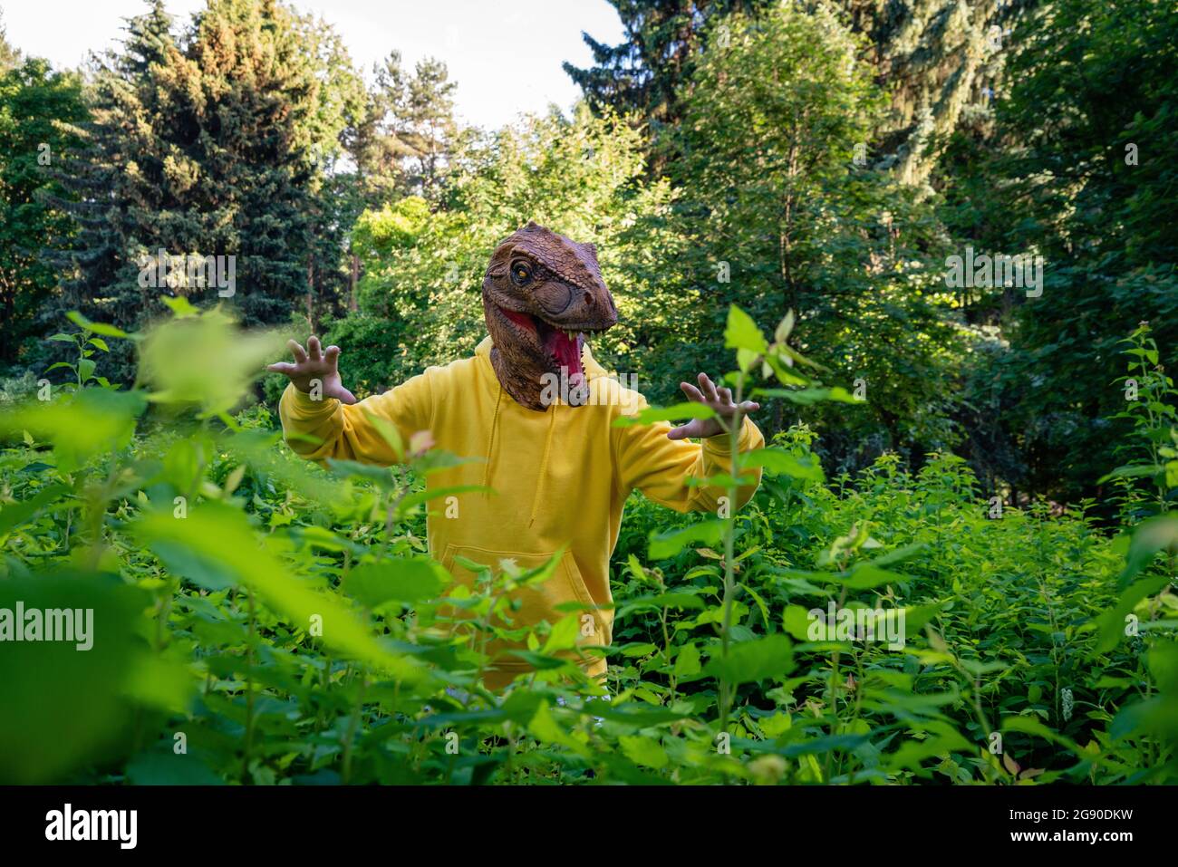 Junge trägt Dinosauriermaske und erschreckt inmitten von Pflanzen Stockfoto
