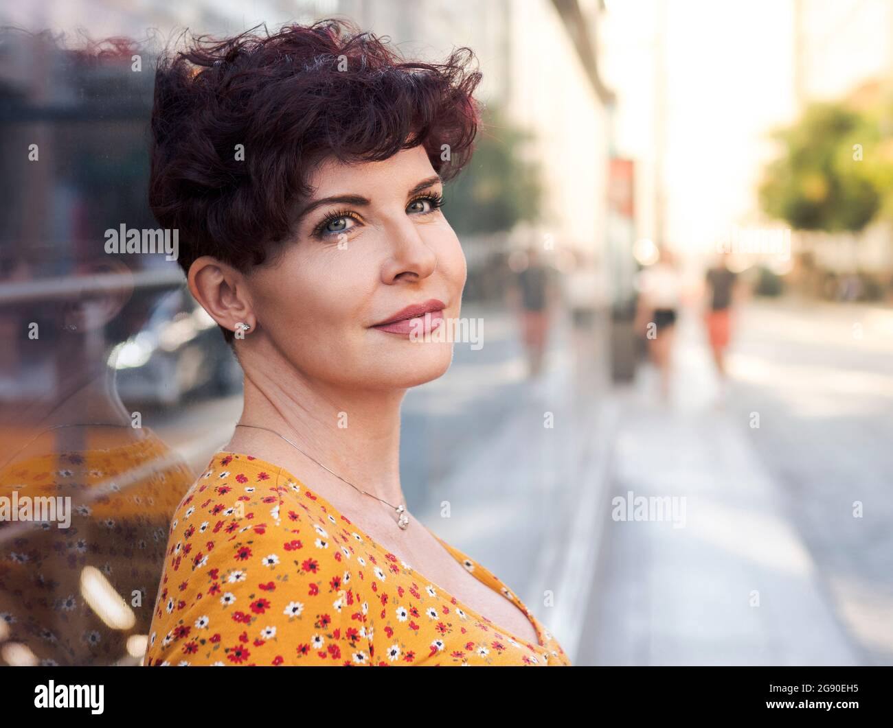 Reife Frau mit kurzen Haaren, die nachdenklich ist, während sie sich an die Wand lehnt Stockfoto