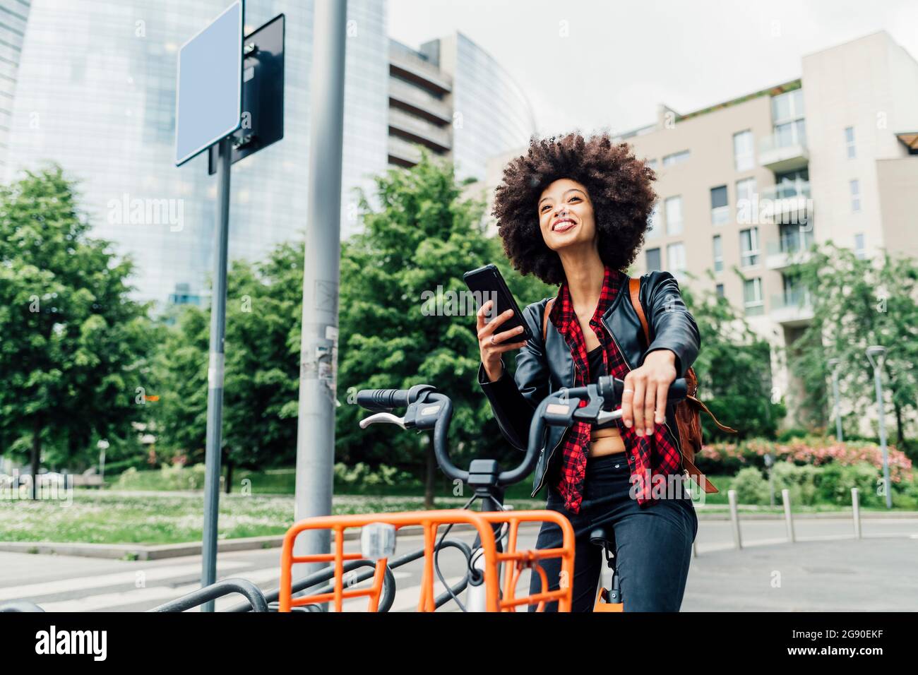 Junge Frau entriegelt das Fahrrad mit dem Smartphone am Parkplatz Stockfoto