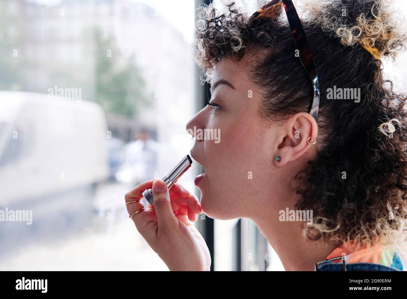 Junge Frau, die Lippenstift im Café anwendet Stockfoto