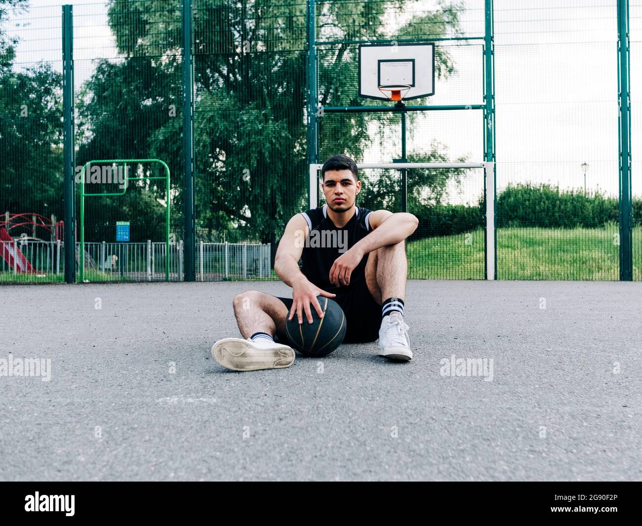 Basketballspieler sitzt mit Ball auf dem Platz Stockfoto
