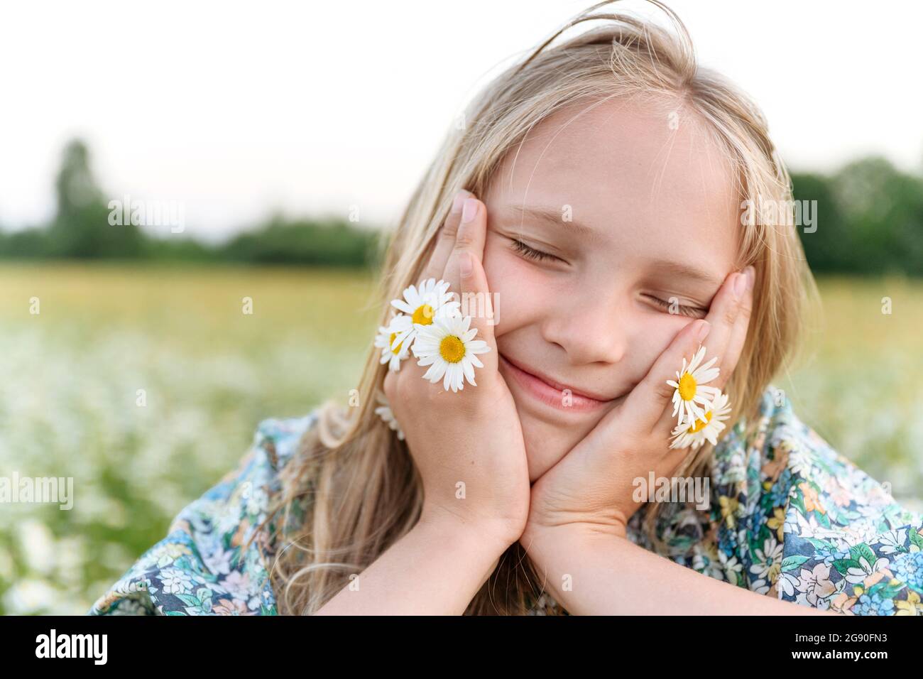 Blonde Mädchen mit Kamillenblumen lächeln, während Tag träumen im Feld Stockfoto