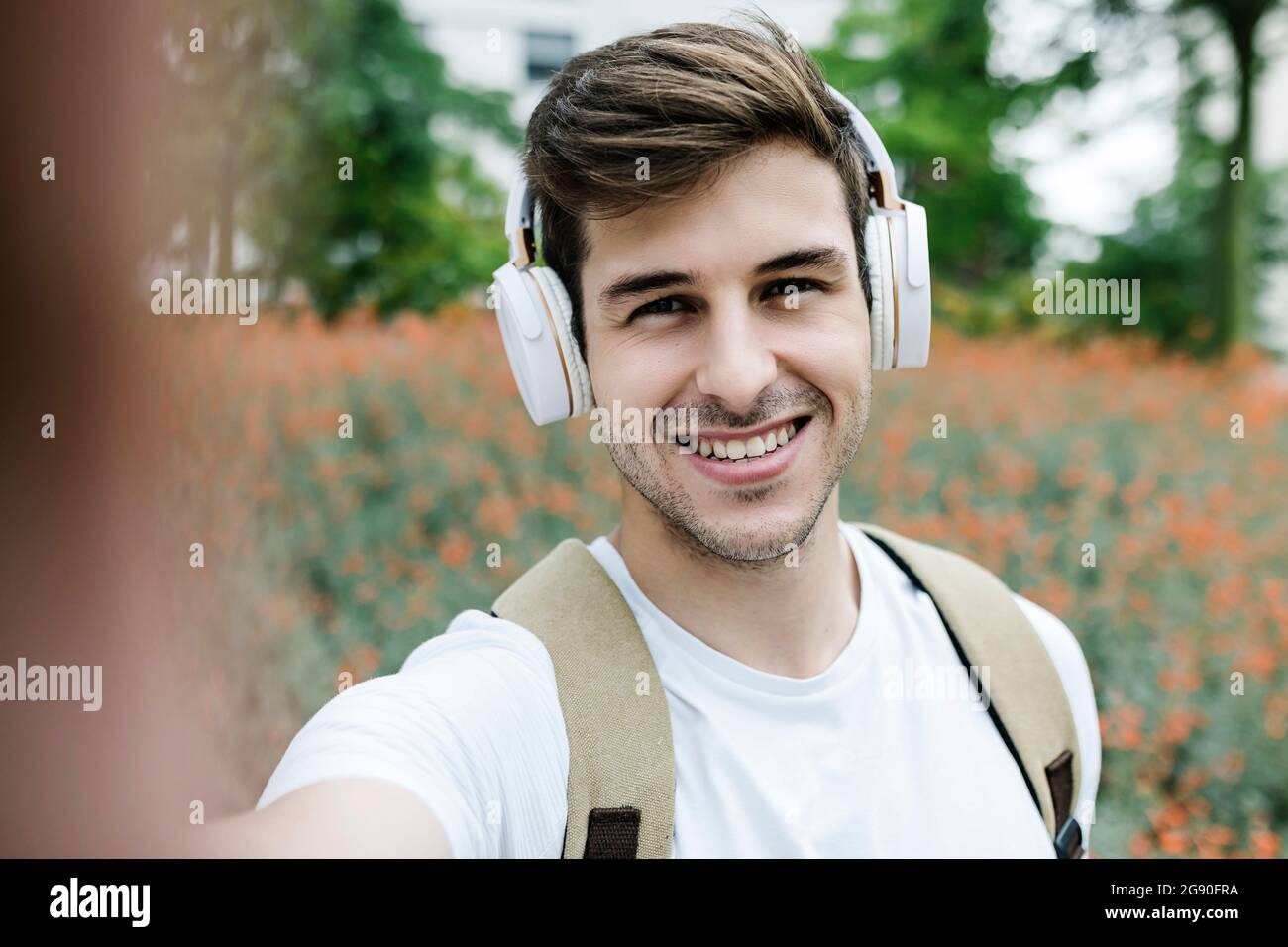 Schöner Mann lächelt, während er Selfie auf der Wiese nimmt Stockfoto