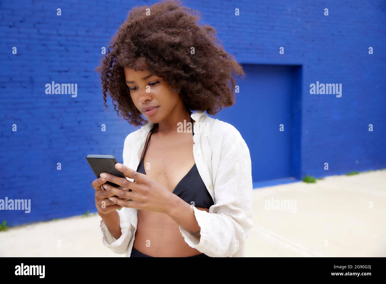 Schöne junge Frau mit braunem Haar mit Smartphone vor der blauen Wand Stockfoto