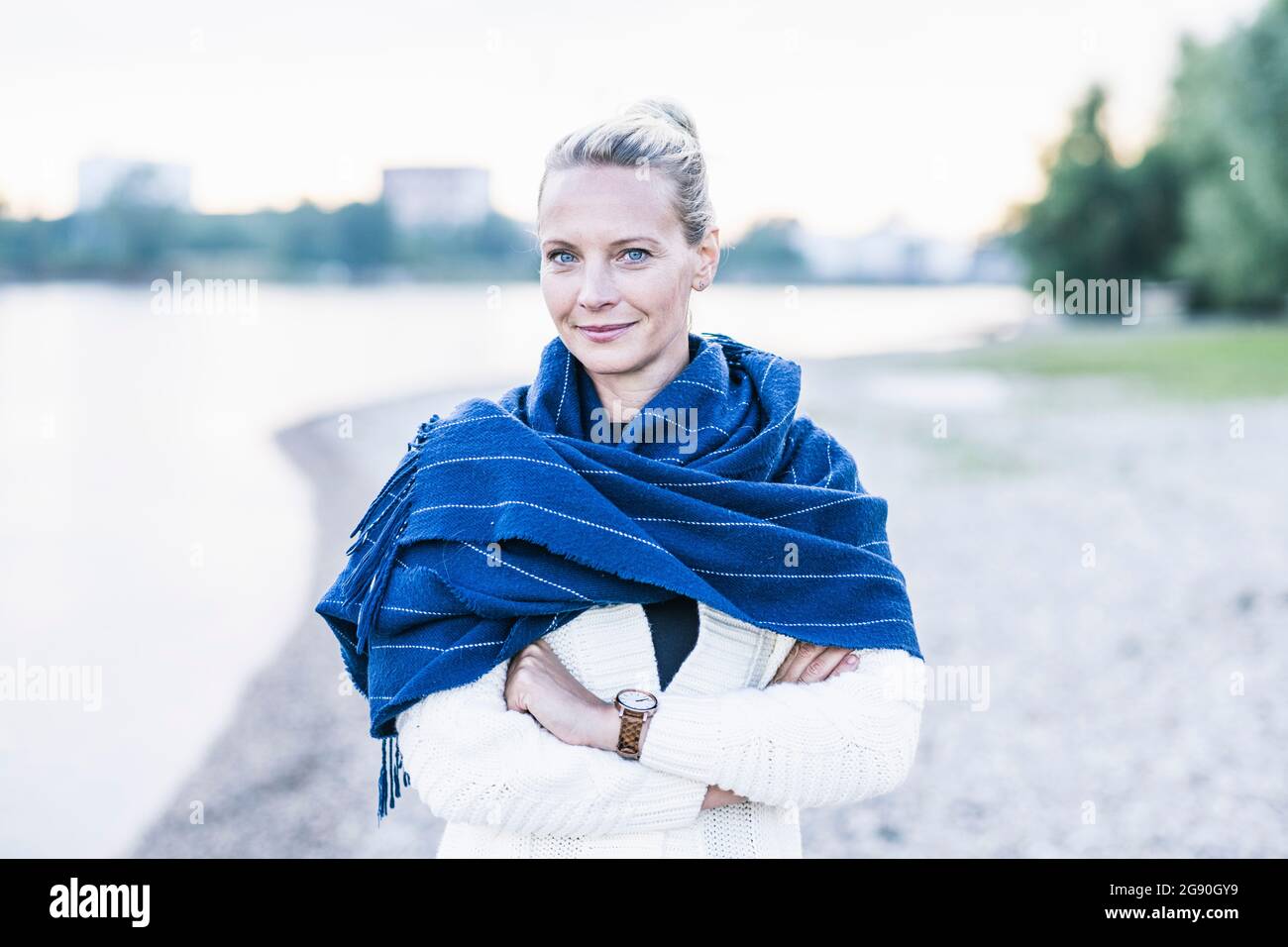 Reife Frau lächelt, während sie mit gekreuzten Armen steht Stockfoto