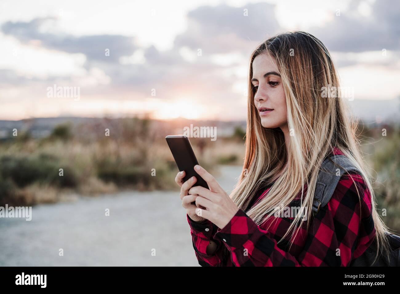 Junge schöne Frau mit blonden Haaren Textnachrichten über Smartphone während des Sonnenuntergangs Stockfoto