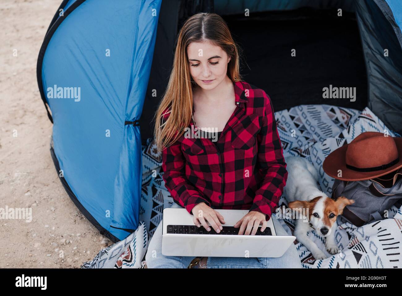 Junge Freiberuflerin mit Laptop, die mit Hund im Zelt sitzt Stockfoto