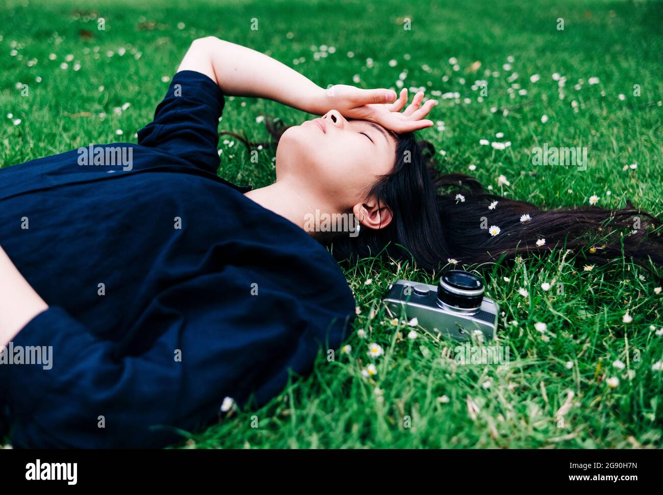 Junge Fotografin mit altmodischer Kamera, die auf Gras ruht Stockfoto