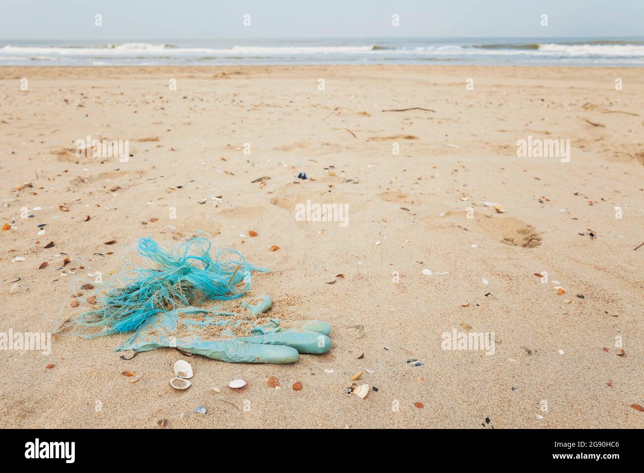 Gebrauchte Einweghandschuh und andere Abfälle verschmutzen sandigen Küstenstrand Stockfoto