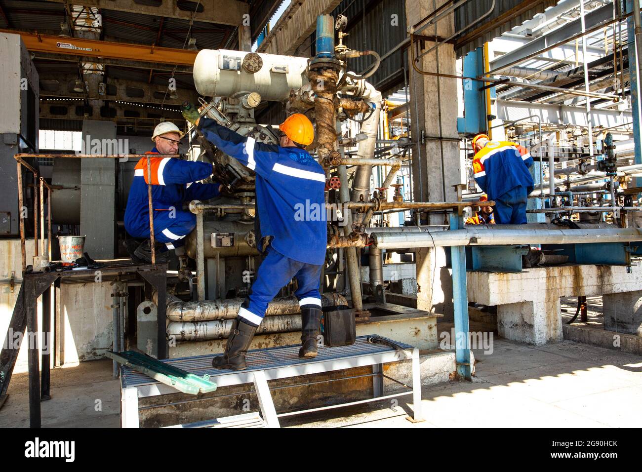 Drei Mechaniker in Uniform befestigen den Kompressor an der Reformierungseinheit während der Wartung der Gasraffinerie Shebelinka in der Region Charkow in der Ostukraine Stockfoto