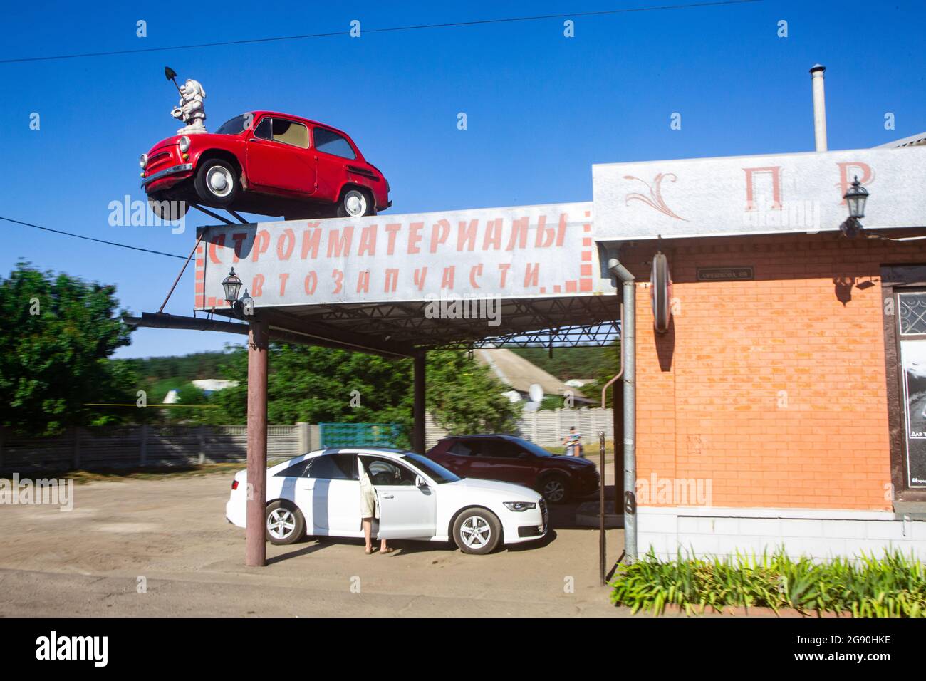 Altes rotes sowjetisches Saporozhets-Auto auf dem Dach von Bauvorräten und Auto-Ersatzteillager in Charkow Industrie-Mega-Stadt im Osten der Ukraine. Stockfoto