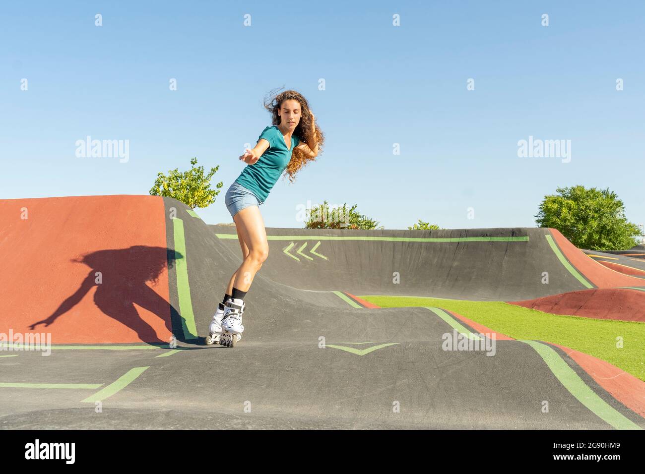 Junge Frau mit der Hand im Haarroller Skating auf Pumptrack während sonnigen Tages Stockfoto
