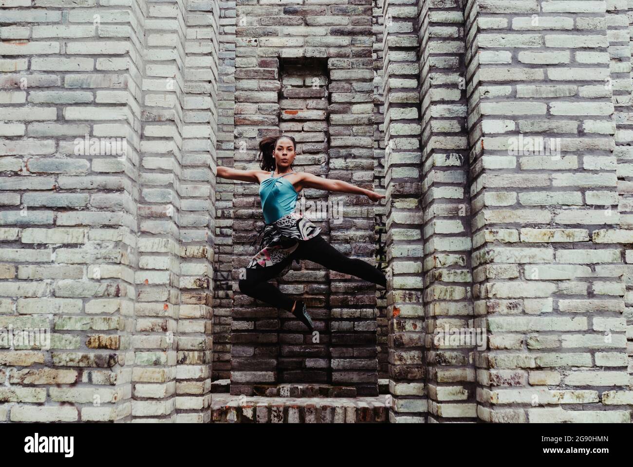 Junge Frau mit ausgestreckten Armen springt vor die Steinmauer Stockfoto