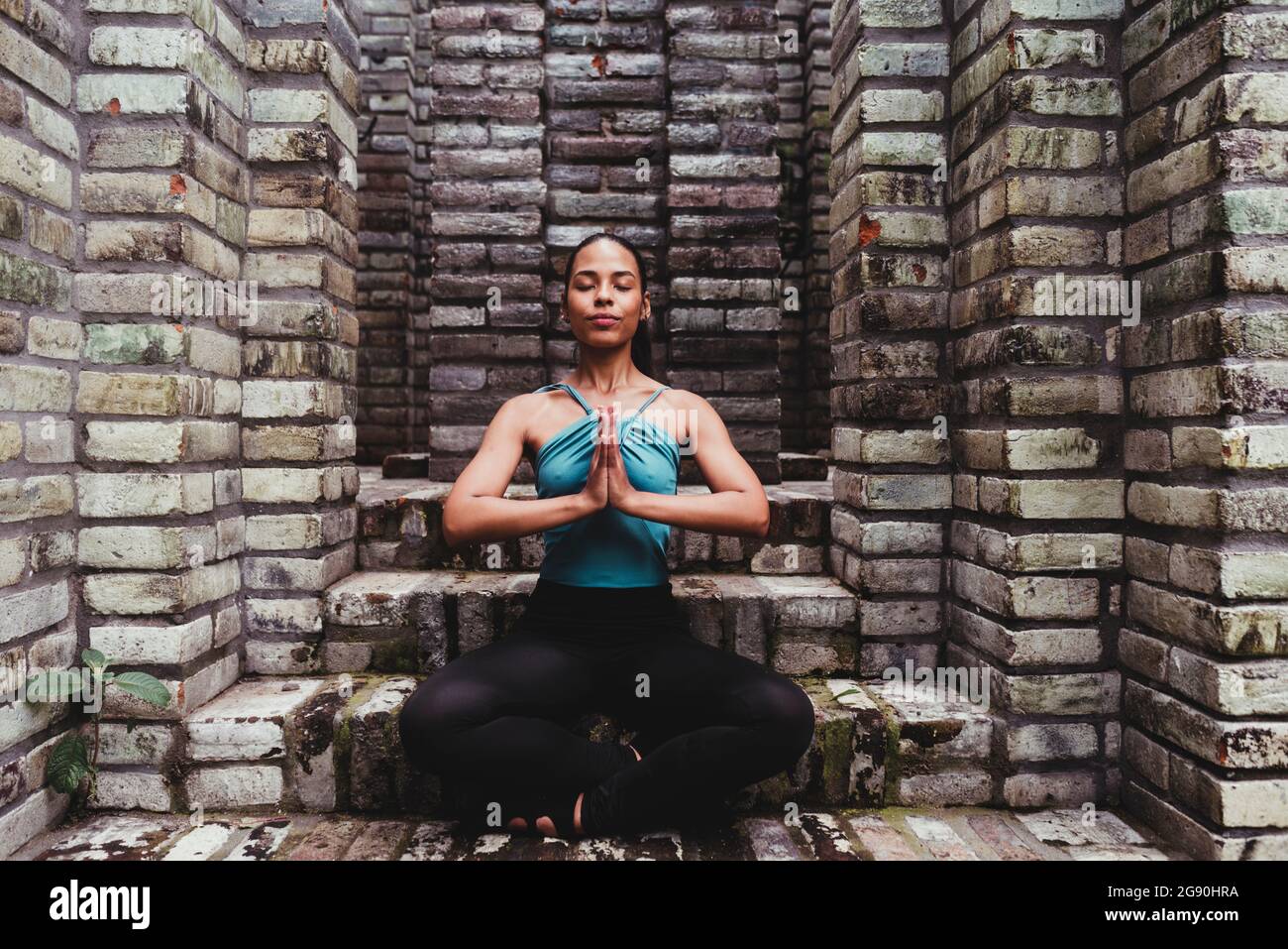 Junge Frau meditiert mit Händen, die in eine Steinstruktur geklammt sind Stockfoto