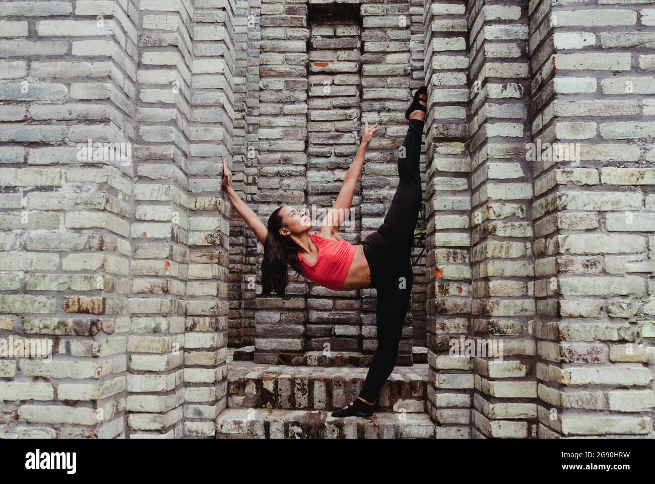 Junge Frau streckt sich das Bein an einer Steinwand Stockfoto