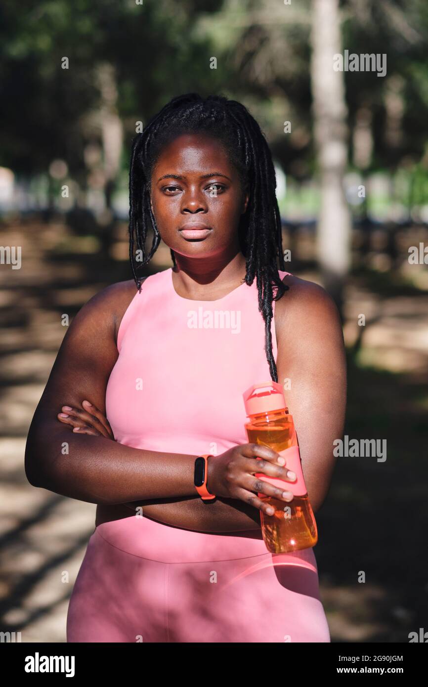 Selbstbewusste junge kurvige Frau mit gekreuzten Armen und Wasserflasche Stockfoto