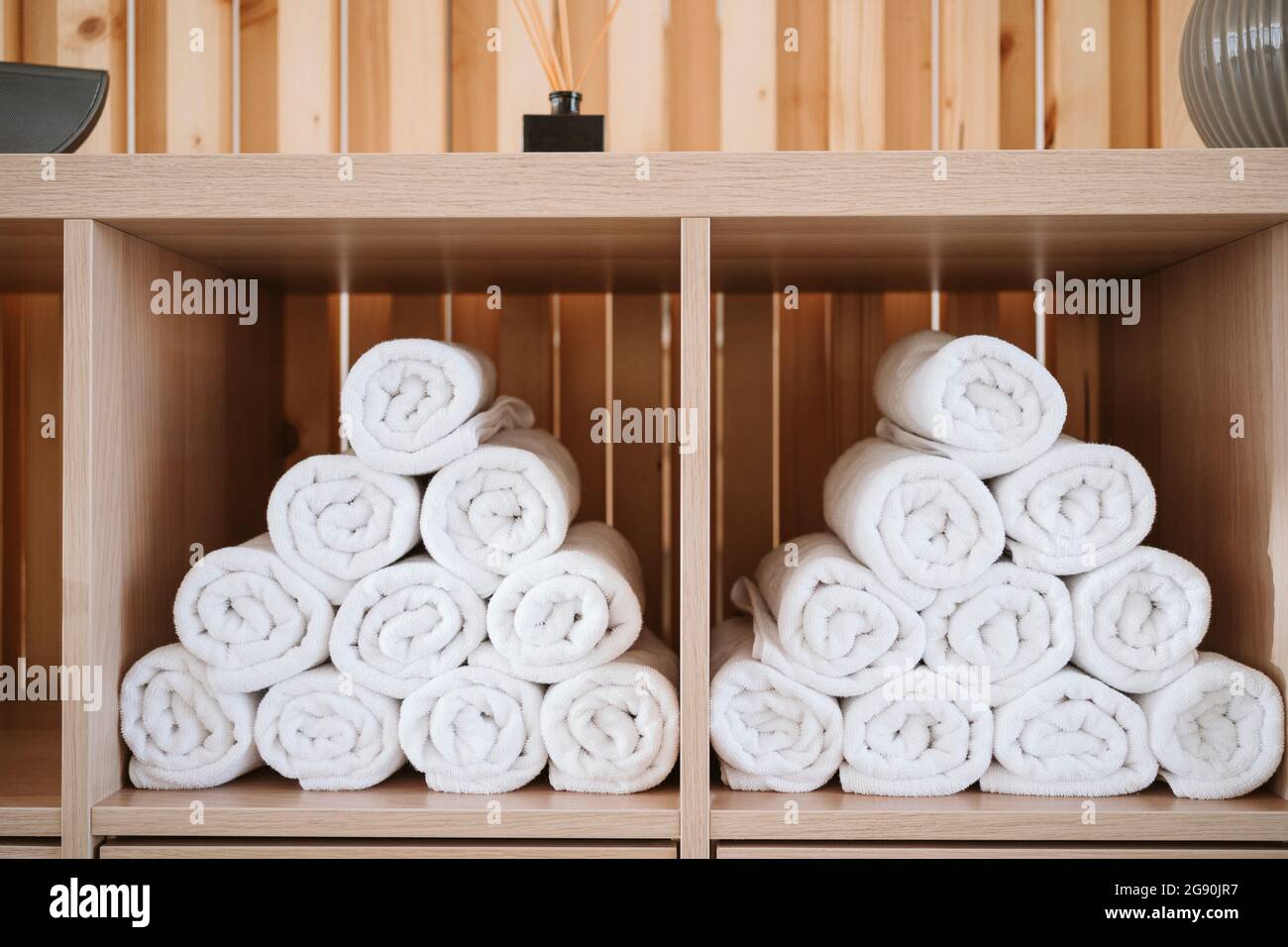 Weiße, zusammengerollte Handtücher, die im Pilates-Studio in einem Holzgestell gestapelt wurden Stockfoto
