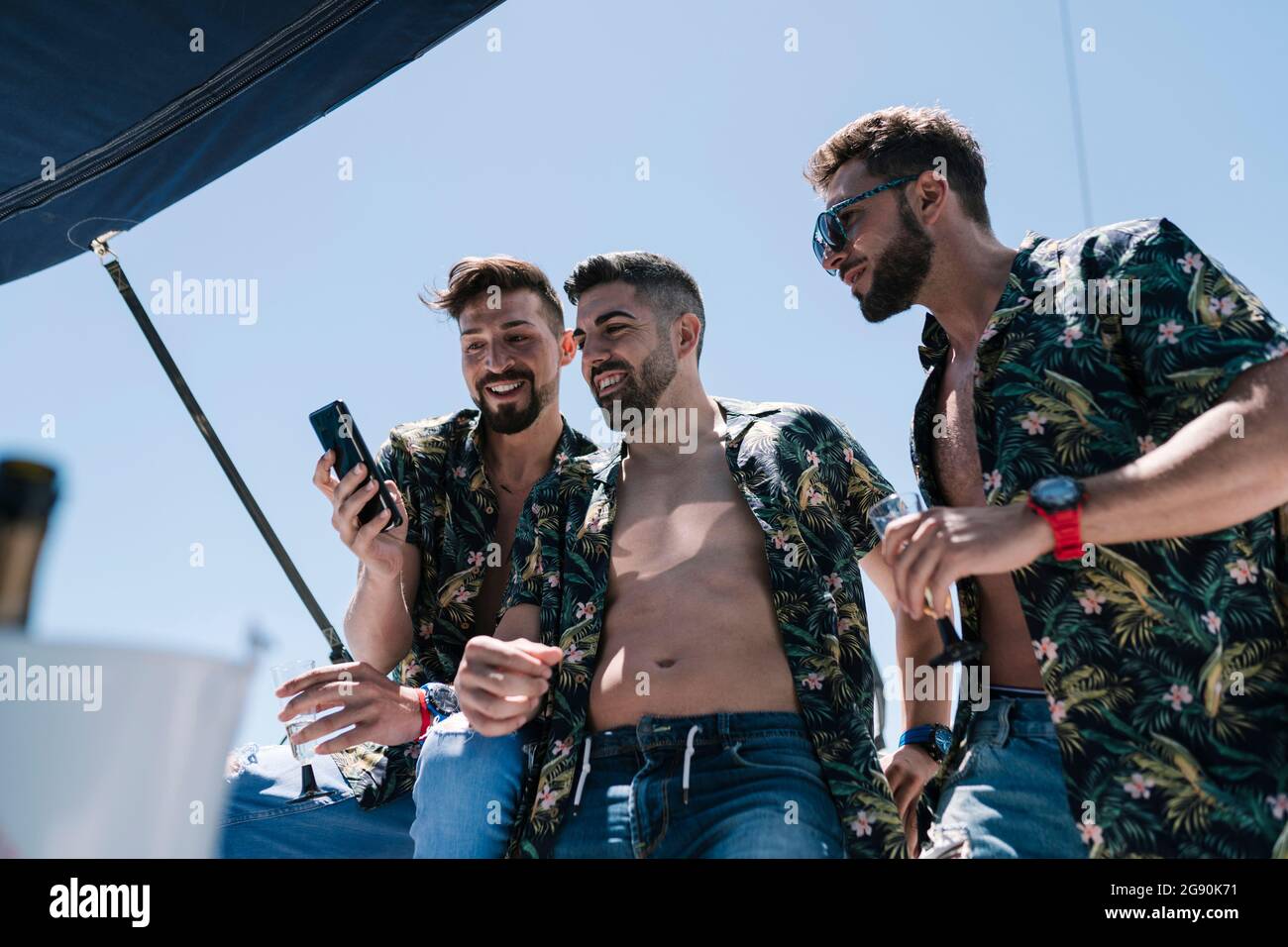 Lächelnder Mann, der während des Urlaubs mit männlichen Freunden auf der Yacht ein Mobiltelefon teilt Stockfoto