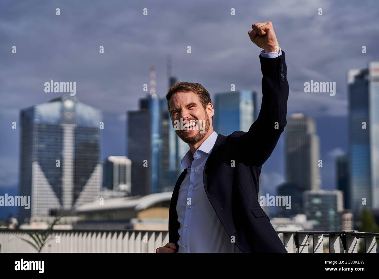 Fröhlicher Geschäftsmann mit erhobener Hand, der auf der Terrasse des Gebäudes feiert Stockfoto