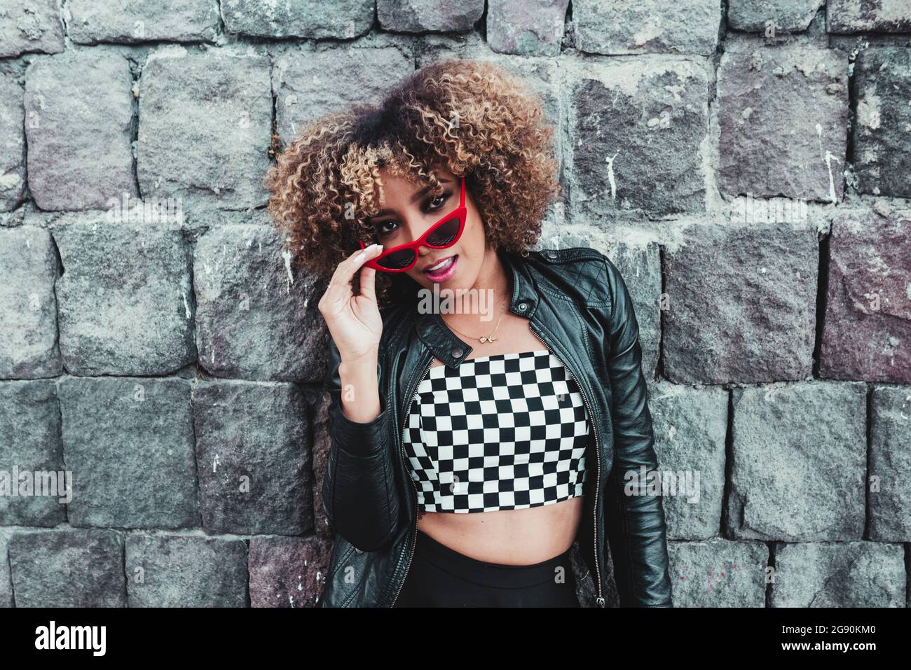 Frau mit Brillen, die vor einer Steinwand stehend auf die Kamera schaute Stockfoto