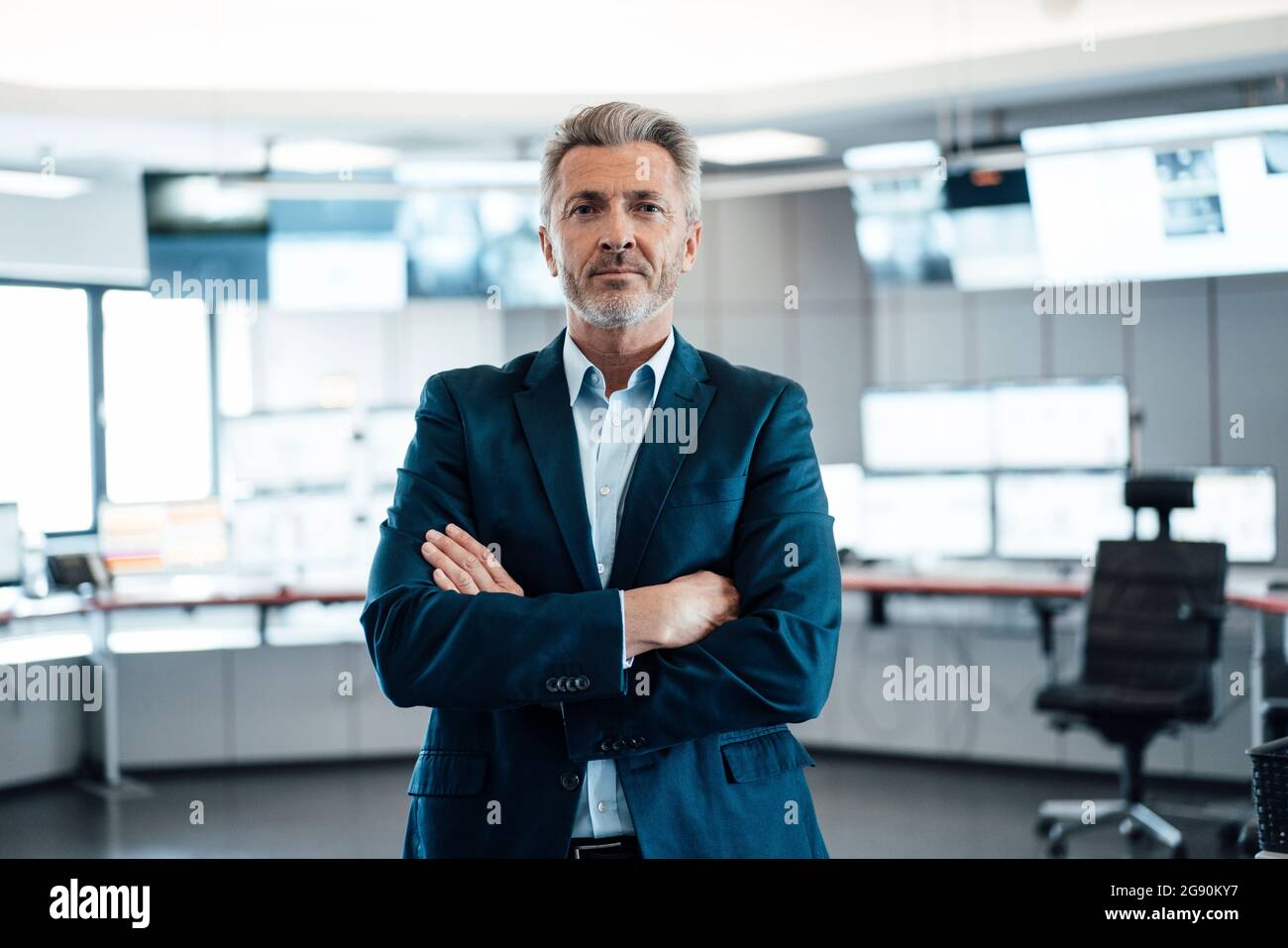 Selbstbewusster Geschäftsmann mit gekreuzten Armen, der im Kontrollraum steht Stockfoto