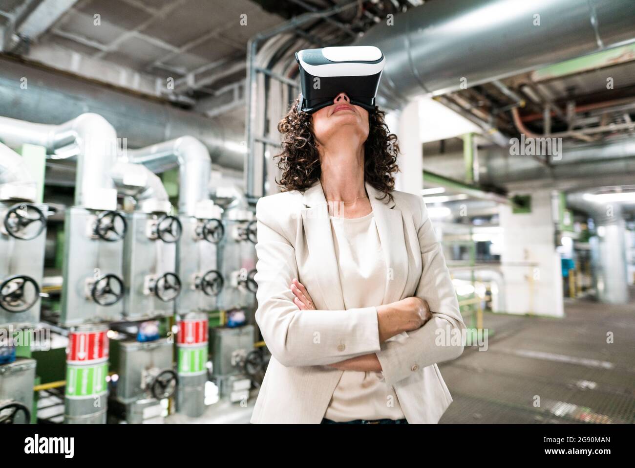 Geschäftsfrau mit gekreuzten Armen mit Virtual-Reality-Headset im Kraftwerk Stockfoto