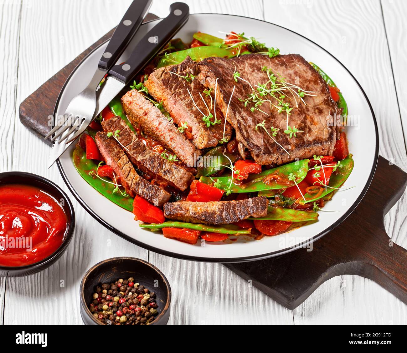 Gegrilltes Rindfleisch-Flankensteak mit Ragout aus geschmorter Tomatensauce, süßem roten Pfeffer, Schneeerbsenschoten, Zwiebeln und Thymian Stockfoto
