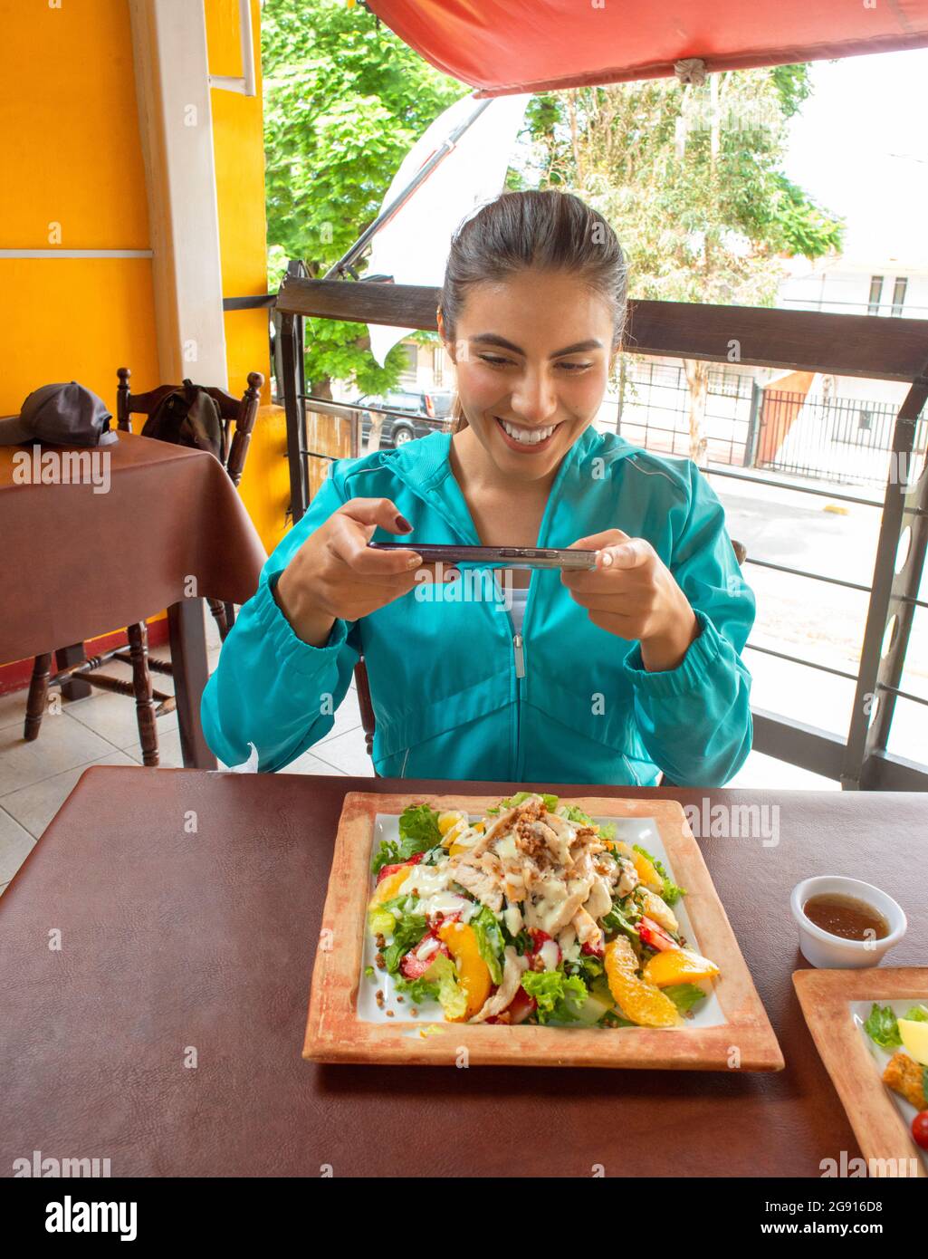 Lateinisches Mädchen lächelt in sportlichem Outfit und fotografiert Salat Stockfoto