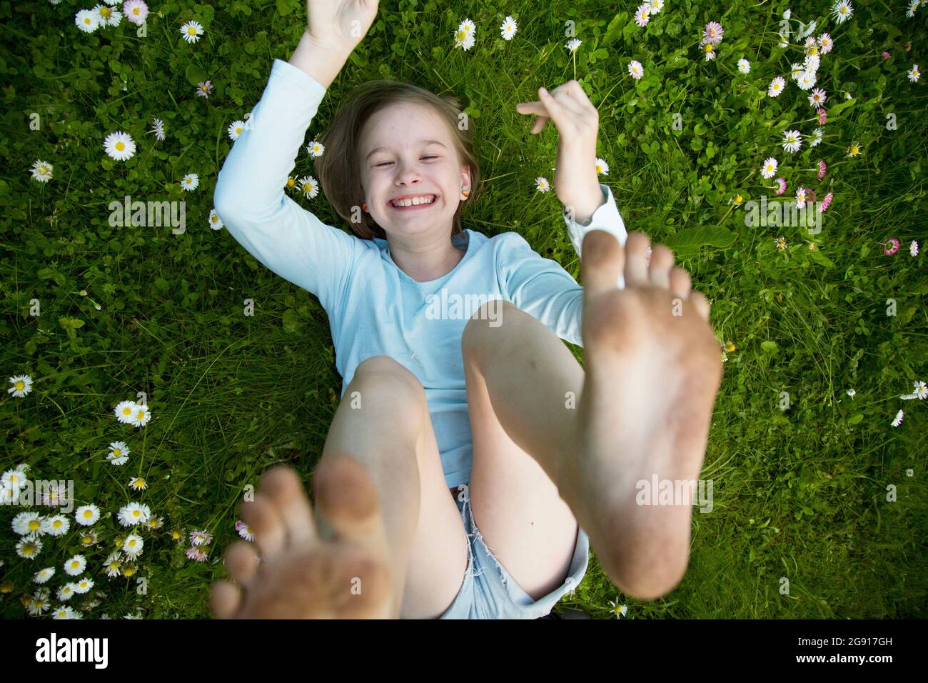 Das Mädchen liegt mit erhobenen Armen und Beinen auf dem Gras. Stockfoto