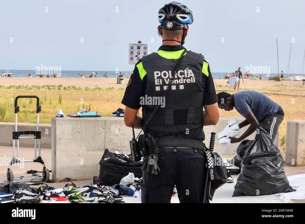 Vendrell, Spanien. Juli 2021. Ein lokaler Polizeibeamter von Vendrell weist  einen illegalen Straßenhändler an, seine Produkte abzuholen und das  Gewerbegebiet zu verlassen. Die örtliche Polizei von Vendrell kämpft wie  jeden Sommer gegen