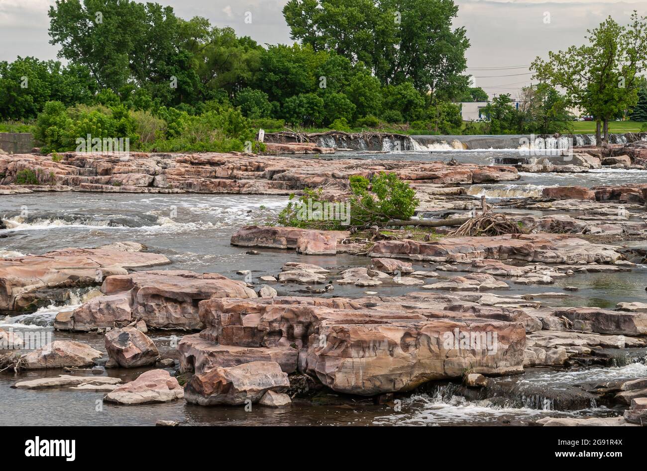 Sioux Falls, SD, USA - 2. Juni 2008: Konzentrieren Sie sich auf die Kaskade von Wasserfällen über beigefarbene Felsen mit etwas grünem Laub im Rücken. Stockfoto