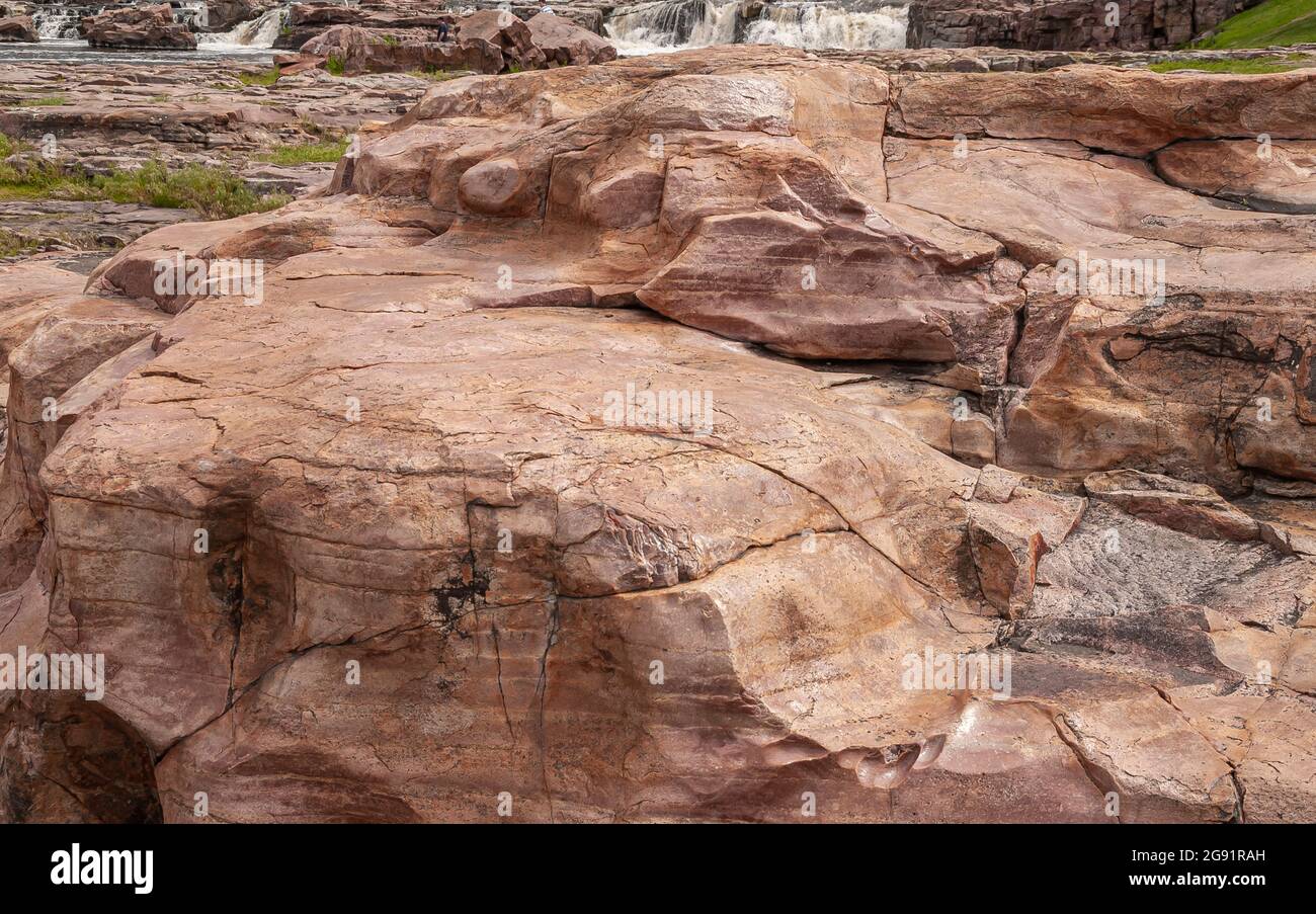 Sioux Falls, SD, USA - 2. Juni 2008: Nahaufnahme eines großen braunen Felsens an einer Kaskade von Wasserfällen. Etwas schäumendes Wasser im Rücken. Polierte Abnutzung auf der Oberfläche Clea Stockfoto