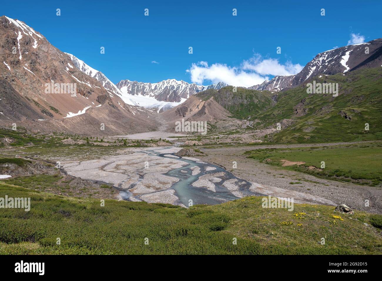 Herrlicher Blick auf den Sommer mit einem gewundenen Fluss zwischen Steinen, Bergen, Gletscher, Bäumen und grünen Hängen vor dem Hintergrund des blauen Himmels und der Wolken Stockfoto