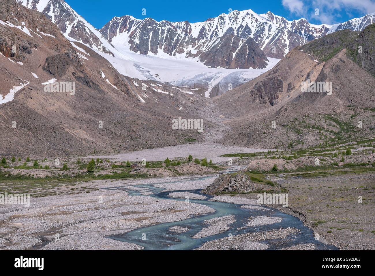 Herrlicher Blick auf den Sommer mit einem gewundenen Fluss zwischen Steinen, Bergen, Gletscher, Bäumen und grünen Hängen vor dem Hintergrund des blauen Himmels und der Wolken Stockfoto