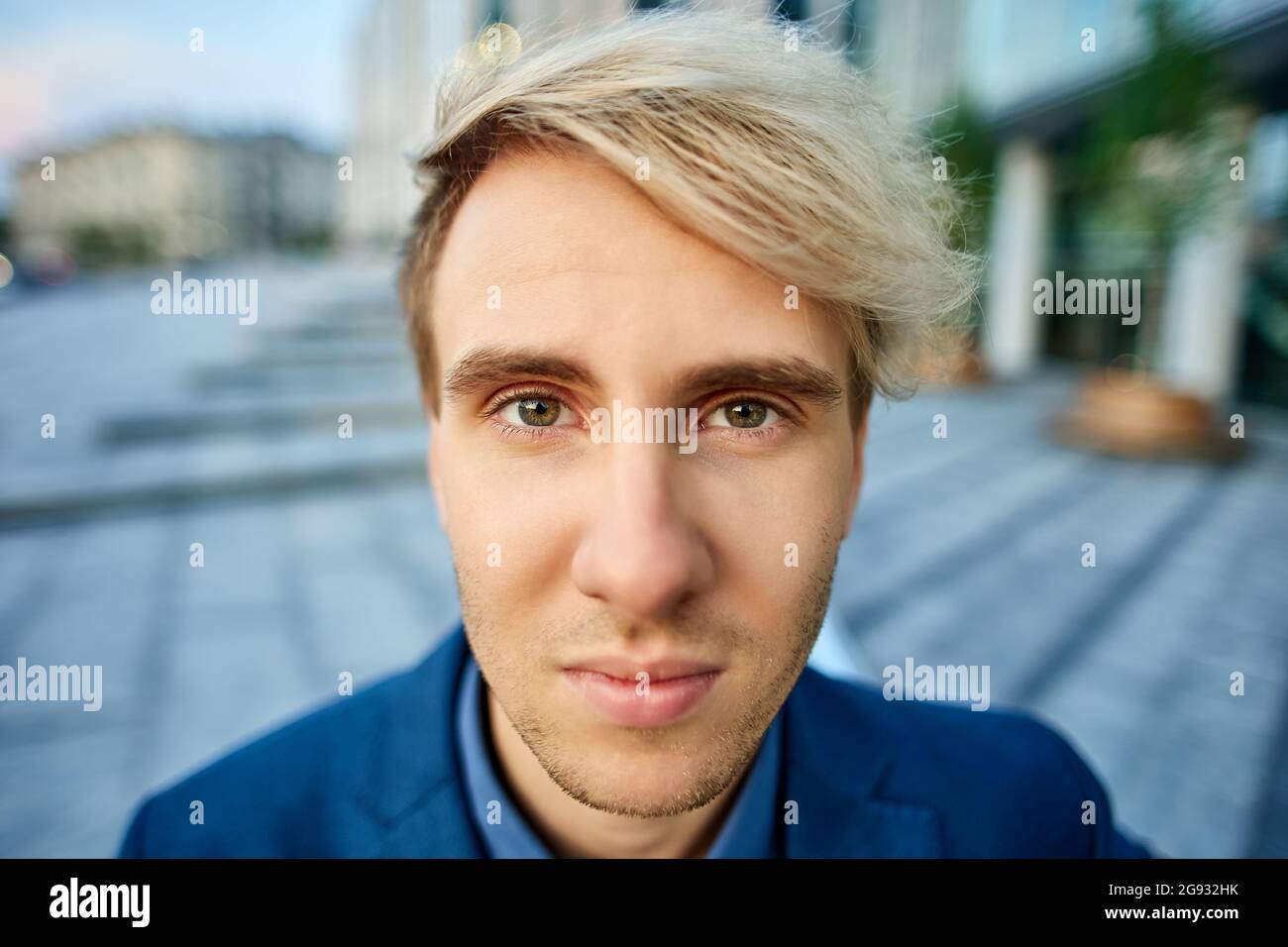 Junger blonder Mann mit ernstem Blick aus der Nähe draußen. Stockfoto