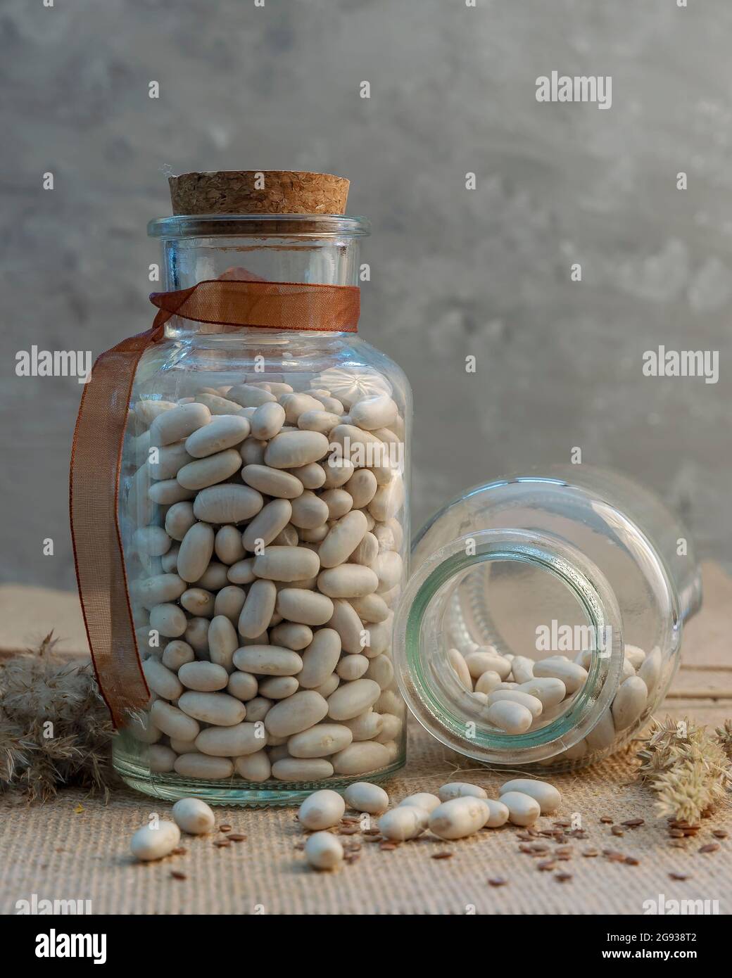 Getrocknete weiße Bohnen in zwei Glasbehältern, von denen einer horizontal auf dem Tisch geöffnet ist Stockfoto