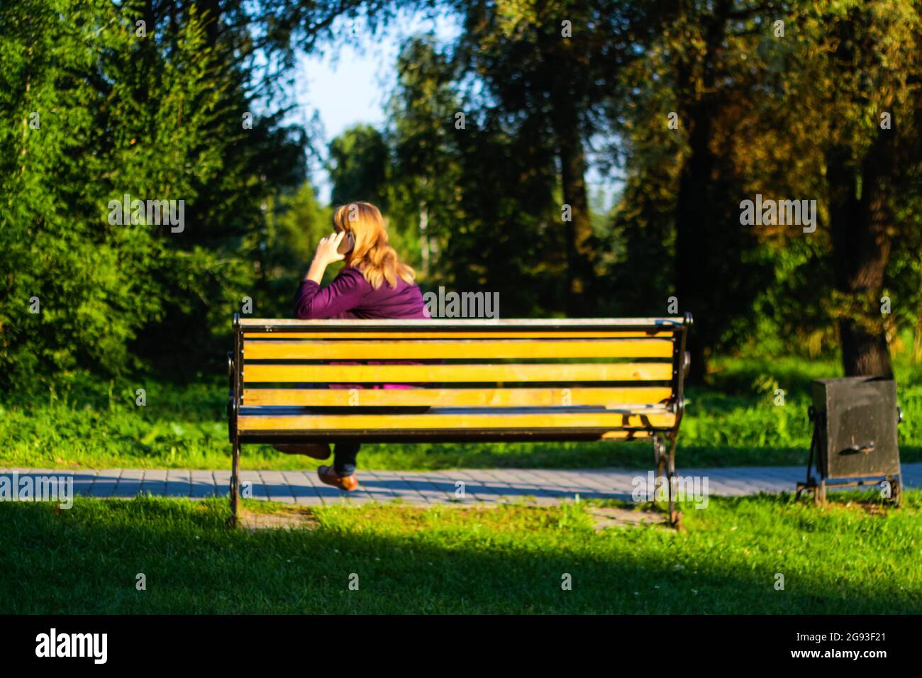 Unschärfe kaukasisch blonde Frau reden, sprechen am Telefon draußen, im Freien. 45er Jahre alte Frau in lila Bluse im Park auf der Bank. Erwachsene Frauen Stockfoto