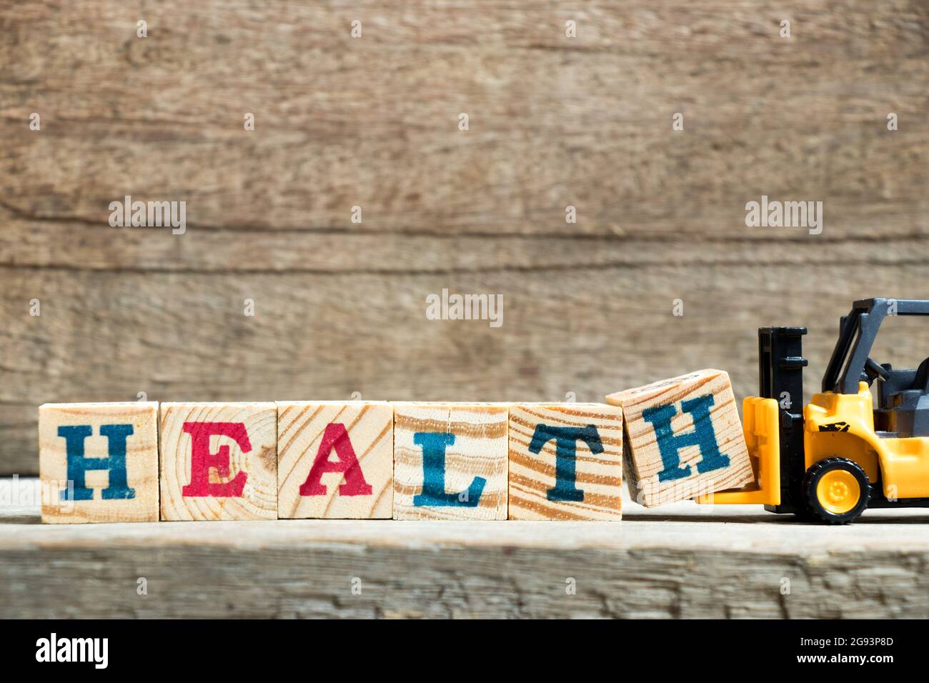 Gelbes Spielzeug Gabelstapler halten Buchstaben Block H, um Wort Gesundheit auf Holz Hintergrund zu vervollständigen Stockfoto