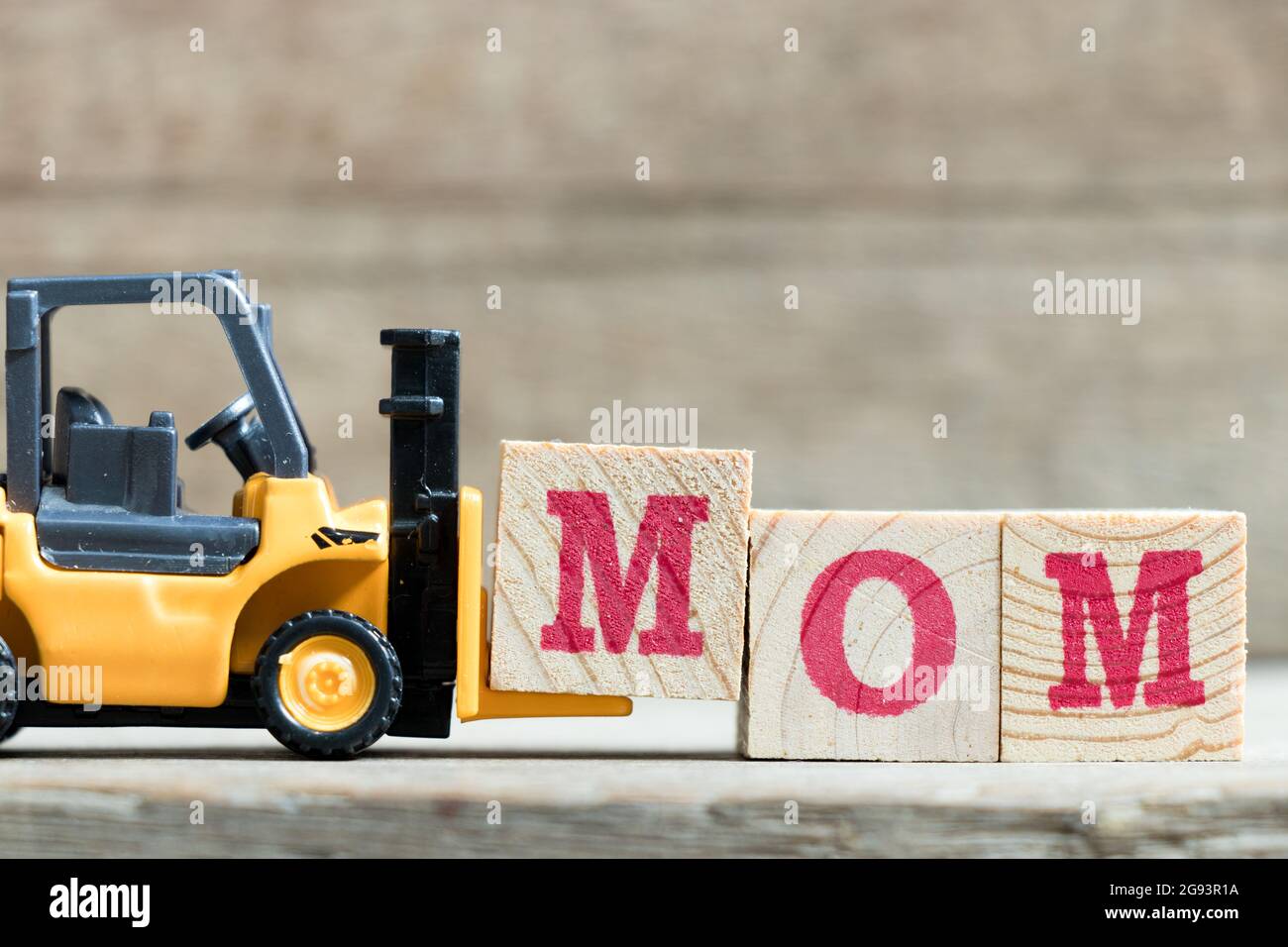 Spielzeug gelb Gabelstapler halten schreiben Block M zu Wort Mama auf Holz Hintergrund komplett (Konzept für Muttertag) Stockfoto
